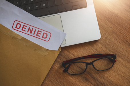 Document with denied stamp on top of laptop on wooden table