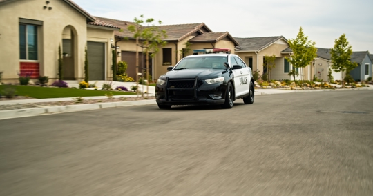 A locked off shot of a police car in a Californian suburb on a mostly clear day in Spring.